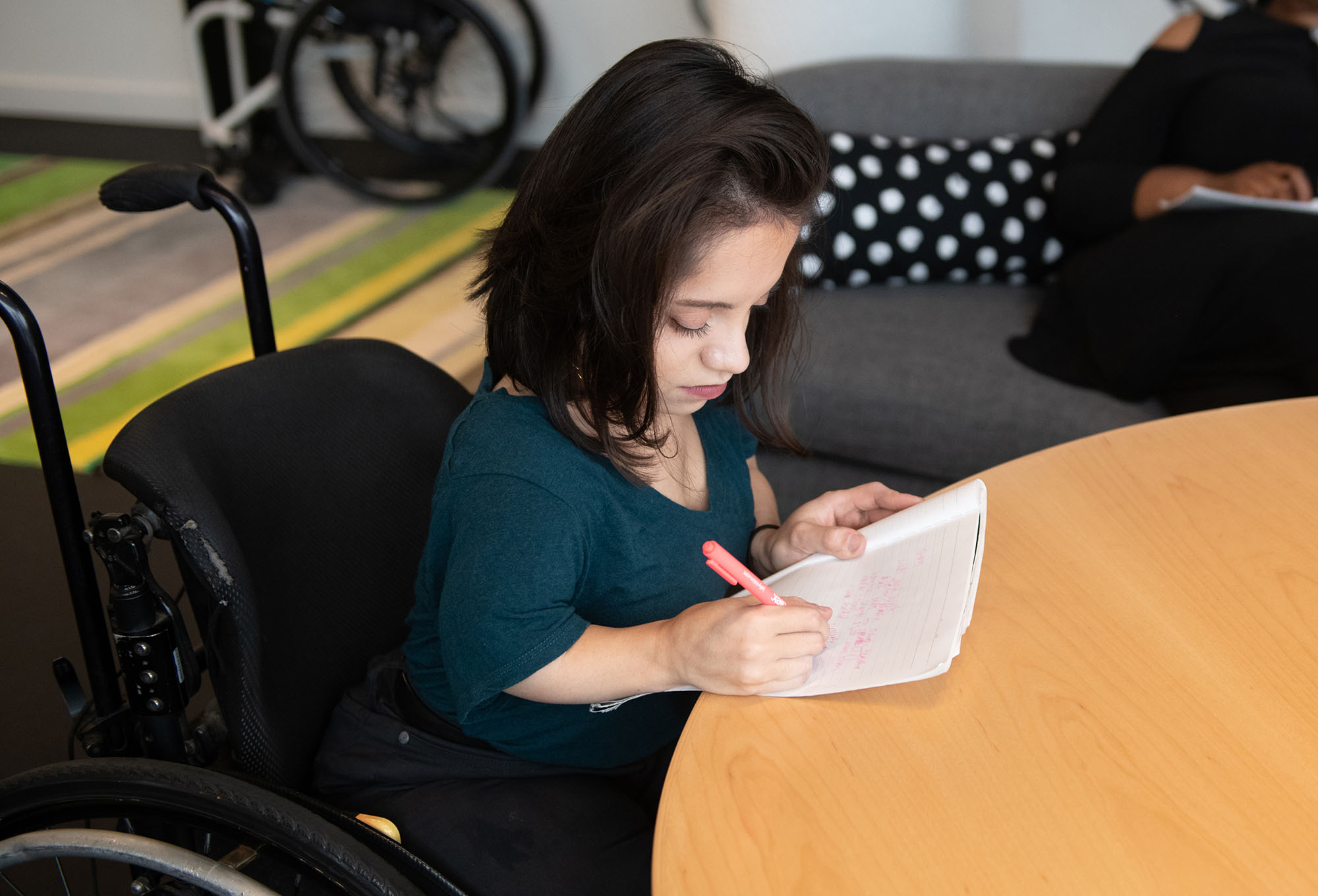 Student in wheelchair writing in a notebook at a desk.