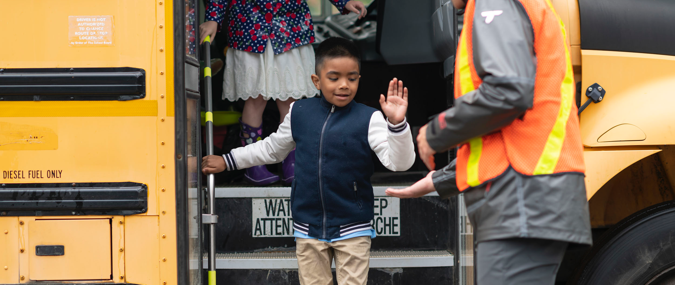 Child stepping out of a school bus to high five a school guard.